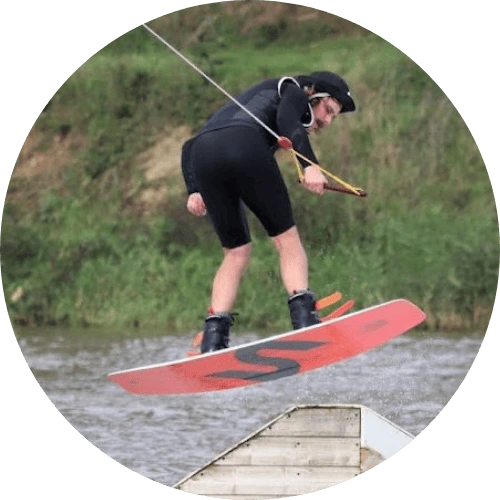 Rider en plein saut au Wakepark de la Rincerie, équipé d’une planche de wakeboard rouge et d’un casque de protection.