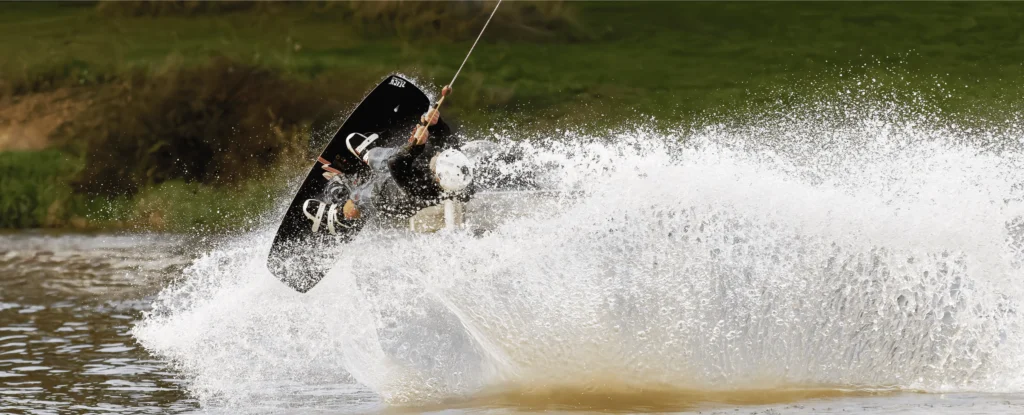 Wakeboarder réalisant une figure aérienne dynamique au Wakepark de la Rincerie, éclaboussures en pleine puissance capturées en noir et blanc.
