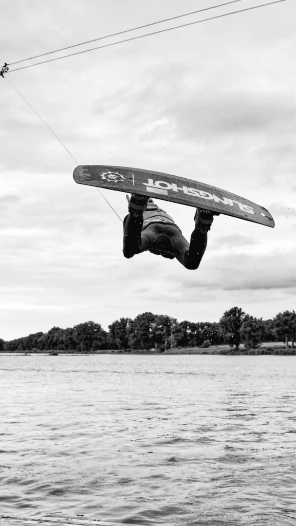 Wakeboarder effectuant une rotation en l'air avec un câble au Wake Park de la Rincerie, en Mayenne, sur fond de paysage naturel.